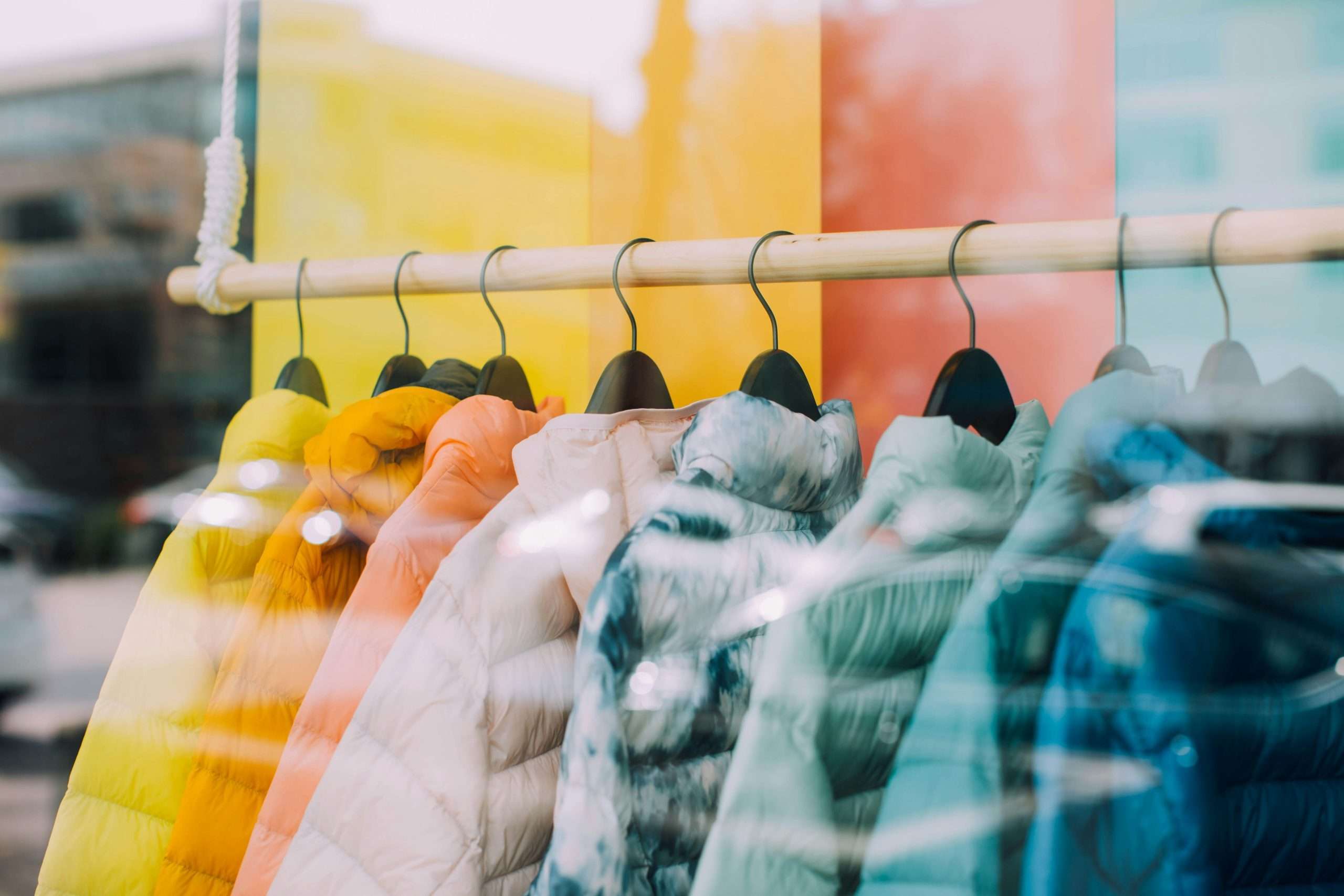 Clothes for sale hanging in a store, seen from outside the window.