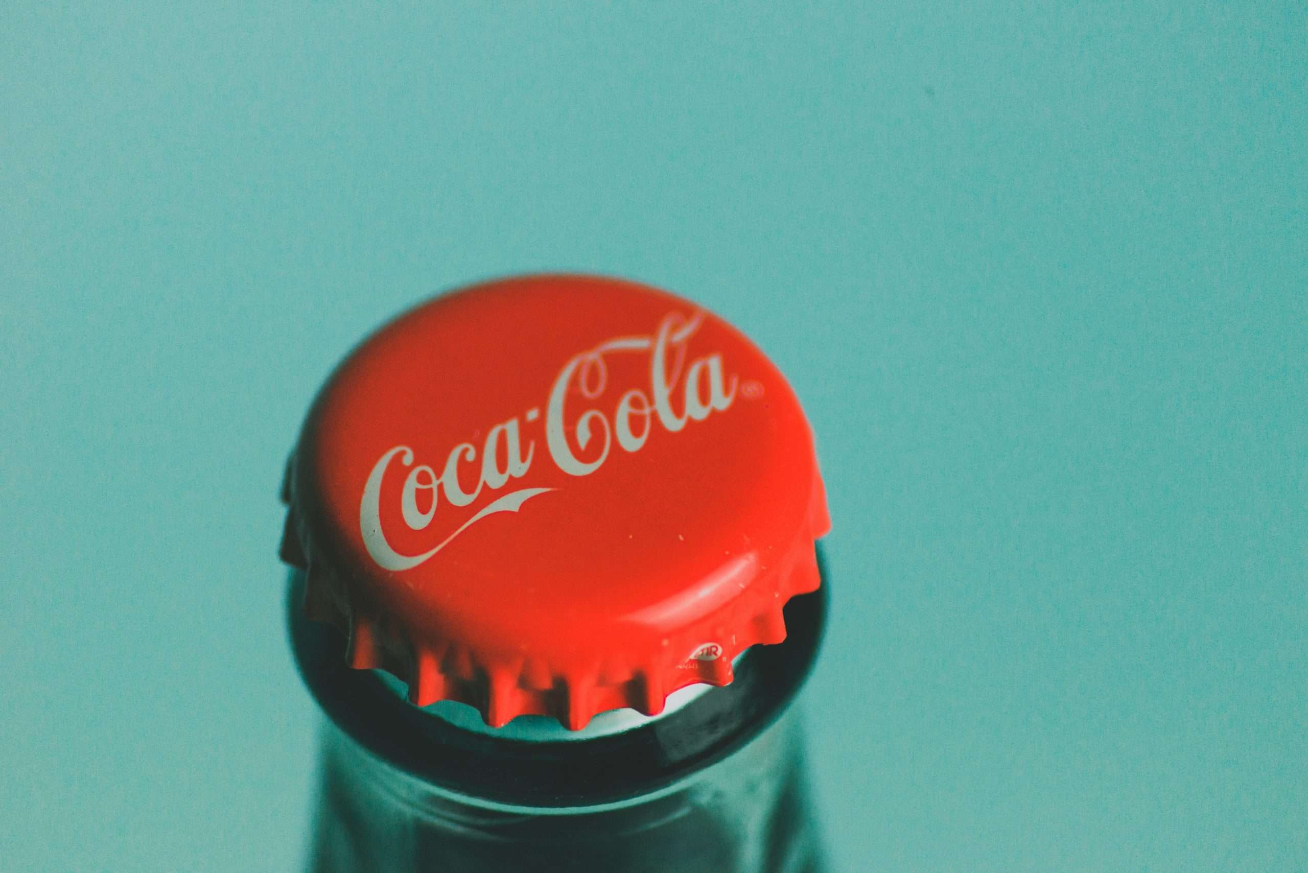 A metal coca-cola bottle top set in front of green background.