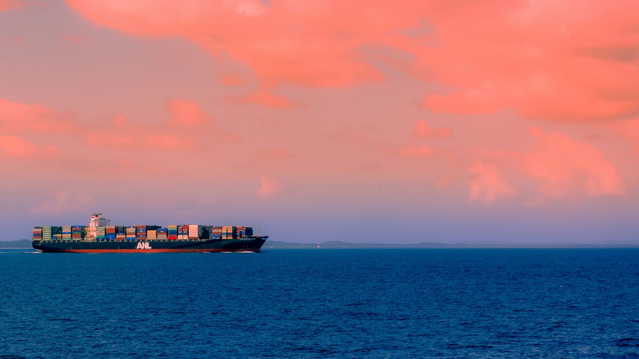 A container ship floating across sea at sunset.