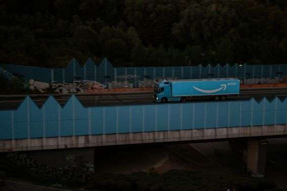 An Amazon lorry travelling along a road in the evening.