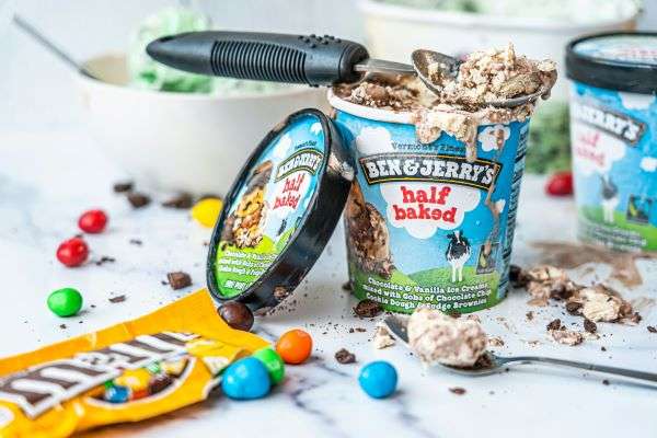 A tub of Ben & Jerry's Half Baked Ice cream opened on a table next to a bag of M&Ms.