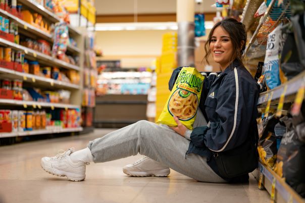 A lady sitting on the floor of a Kroger store eating chips.