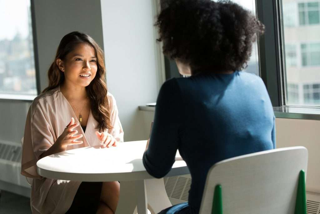 Two Asian businesswomen talking at a table in an office.