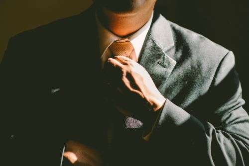 The shoulders and upper body of a business man straightening a tie.