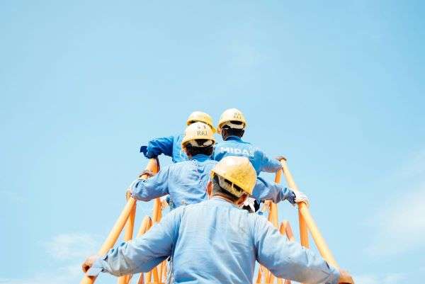 A number of contractors ascending a yellow steel bridge walkway on a construction site.