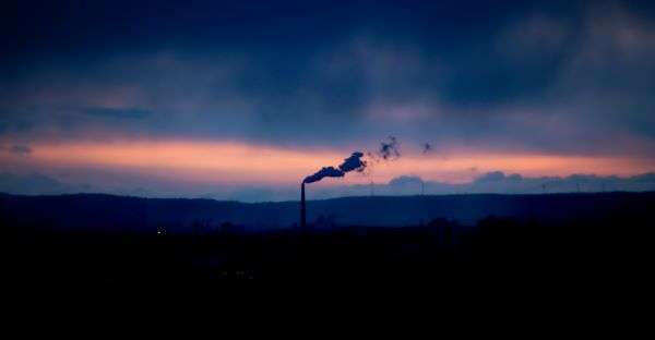 A factory chimney seen at dusk emitting smoke.