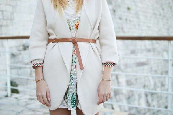 The mid-section of a lady wearing a dress with white cardigan and belt.