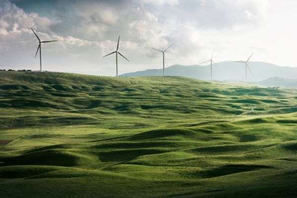 Windmills seen on a hill from a distance set against a cloudy sky.