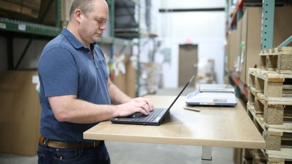 A warehouse worker on a laptop within large storage area of warehouse.