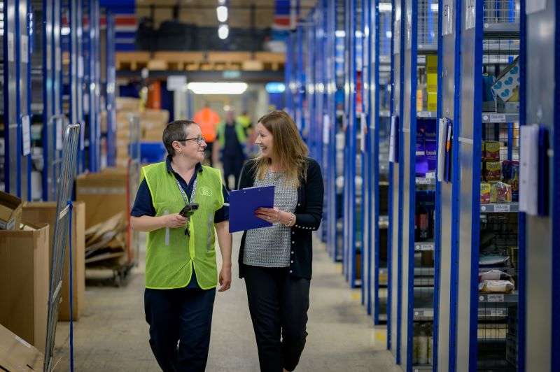 Two females warehouse workers walking along a warehouse aisle.