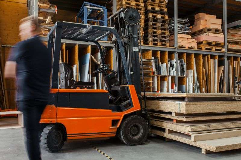 A warehouse working standing beside a forklift.