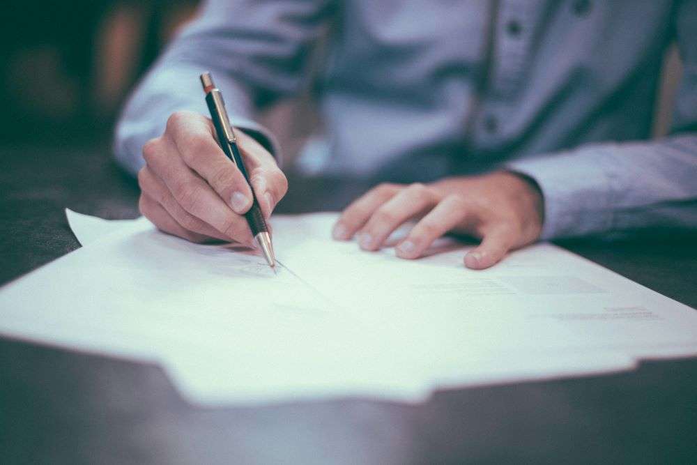 Person writing at a table, representing change to De Mimis. As legislative pressures mount, the possible elimination of the de minimis rule could significantly reshape how e-commerce businesses operate.